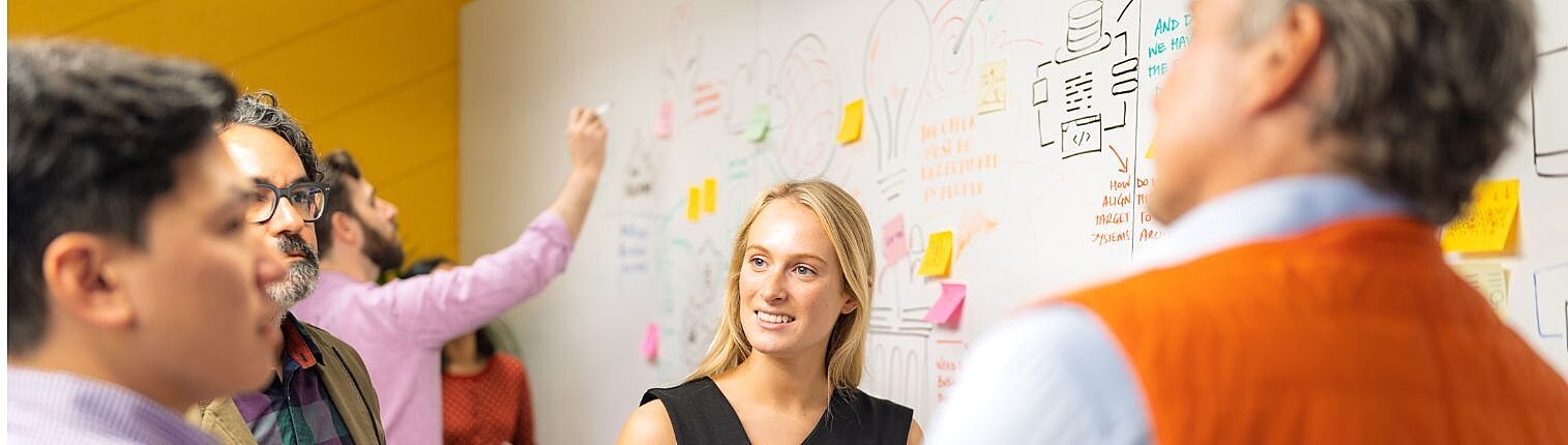 Group of four Nousers talking in a small group next to whiteboard