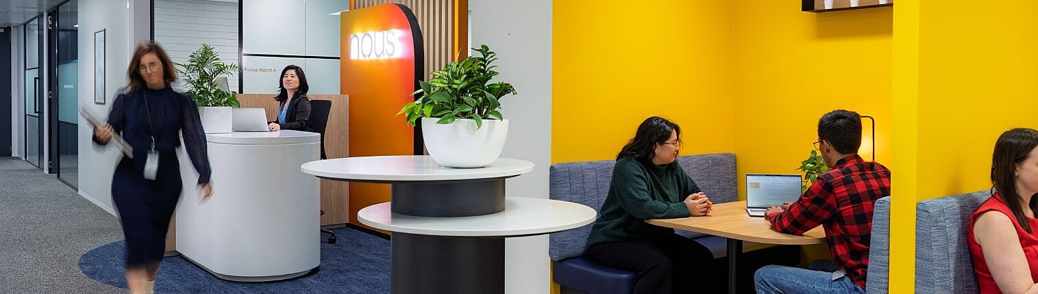 Modern Nous office interior featuring branded reception area, hallway, and collaborative yellow booth seating with professionals working.