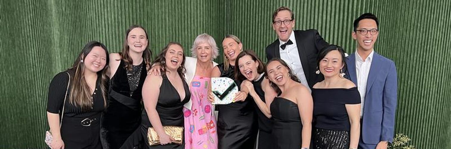 Ten Nous employees standing dressed in formal attire, holding a Good Design Award trophy and smiling at the camera.