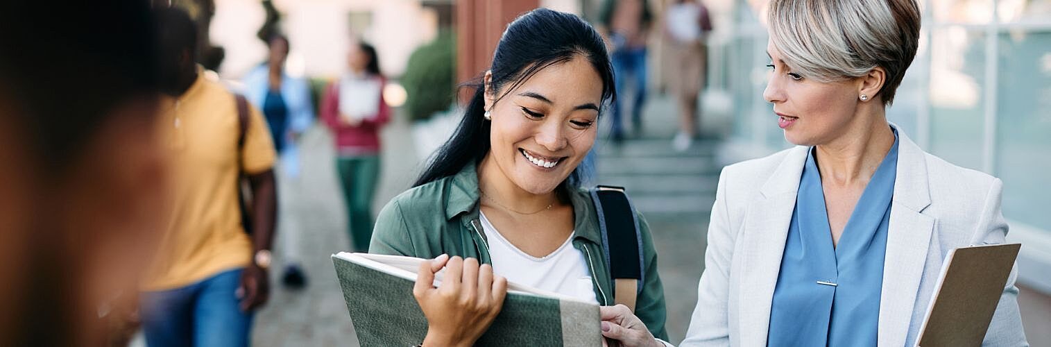Female teacher and female university student discuss something as they walk together.