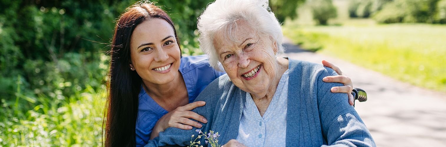 Caregiver and senior woman in wheelchair picking wild flowers.