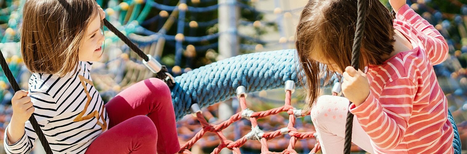 Two little girls swinging at the playground on a summer day.