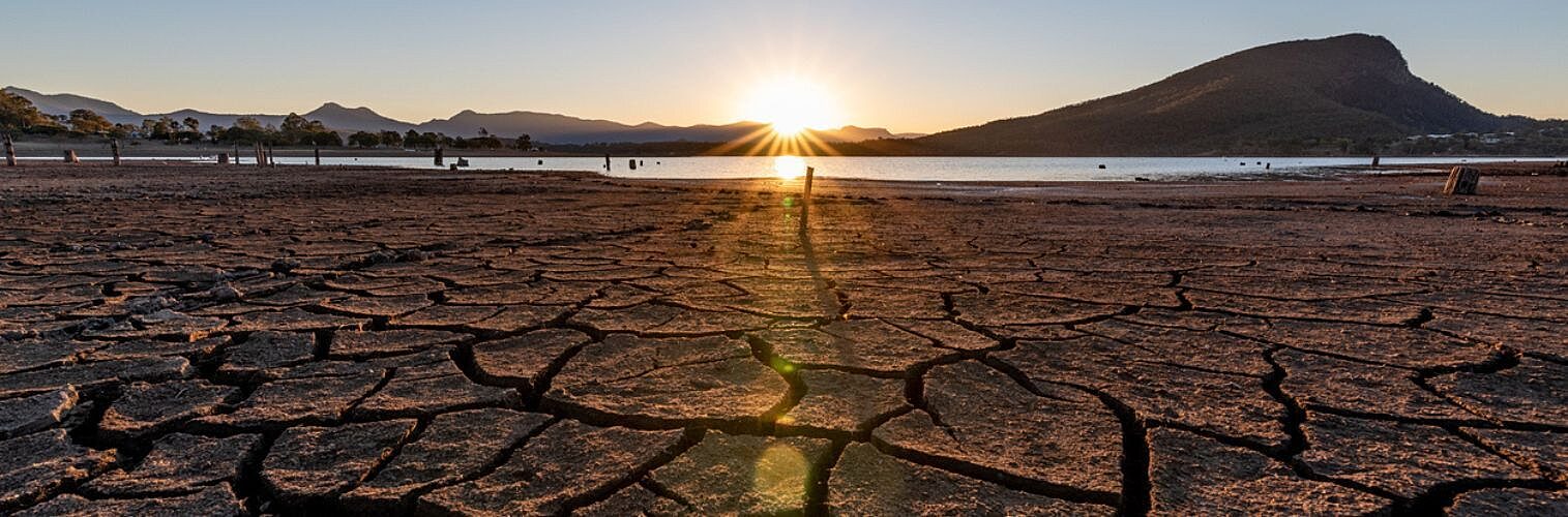 The sun sets setting over a dried, cracked lake bed.