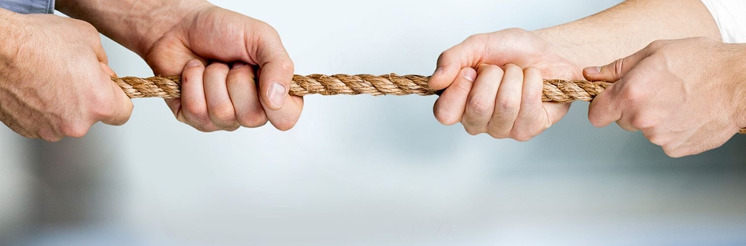 Business people pulling rope in opposite directions at office.