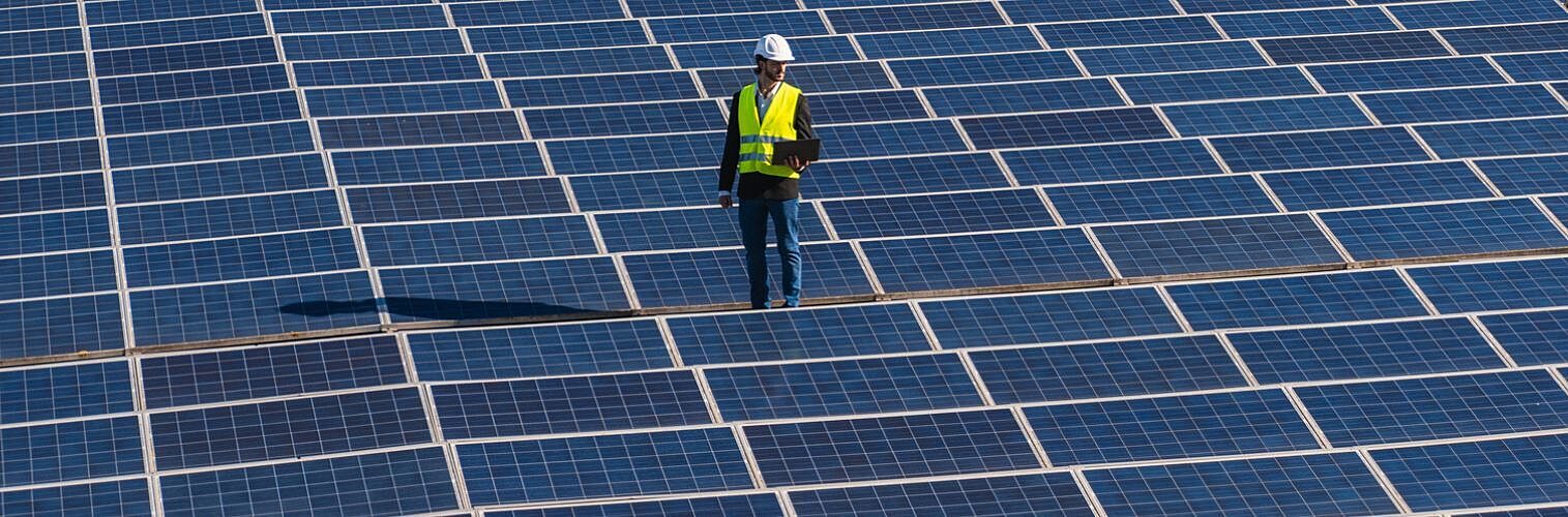 An engineer wearing hard hat and safety vest standing on a solar panel field.