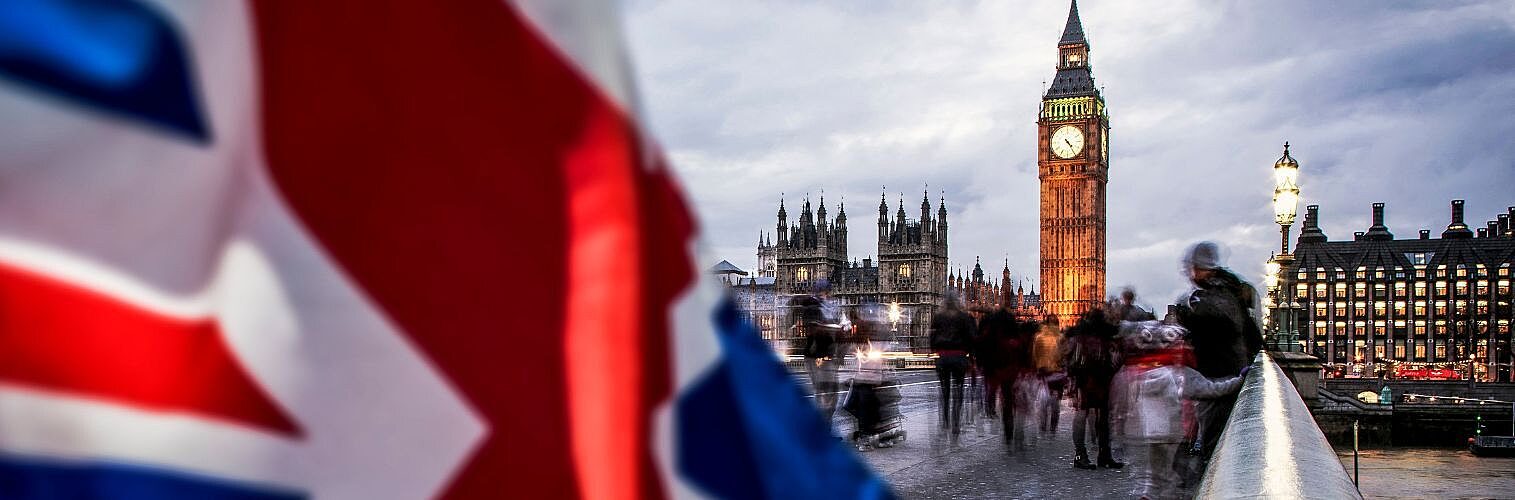 A Union Jack fluttering in front of Big Ben on a bridge.