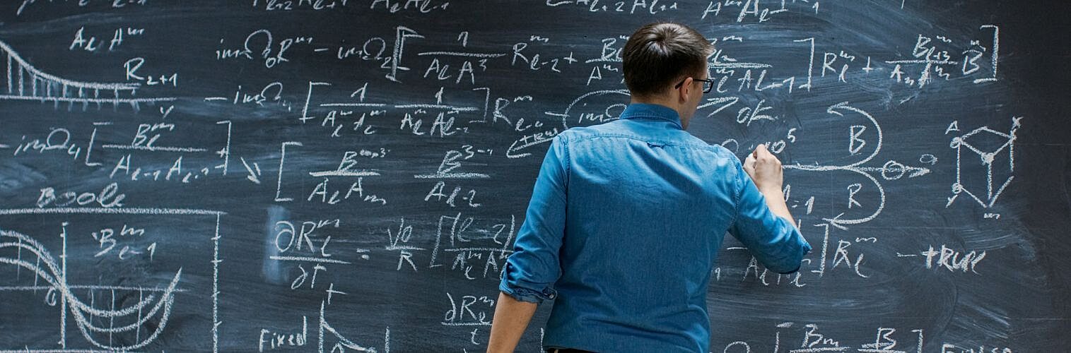 Young mathematician writing on big blackboard.