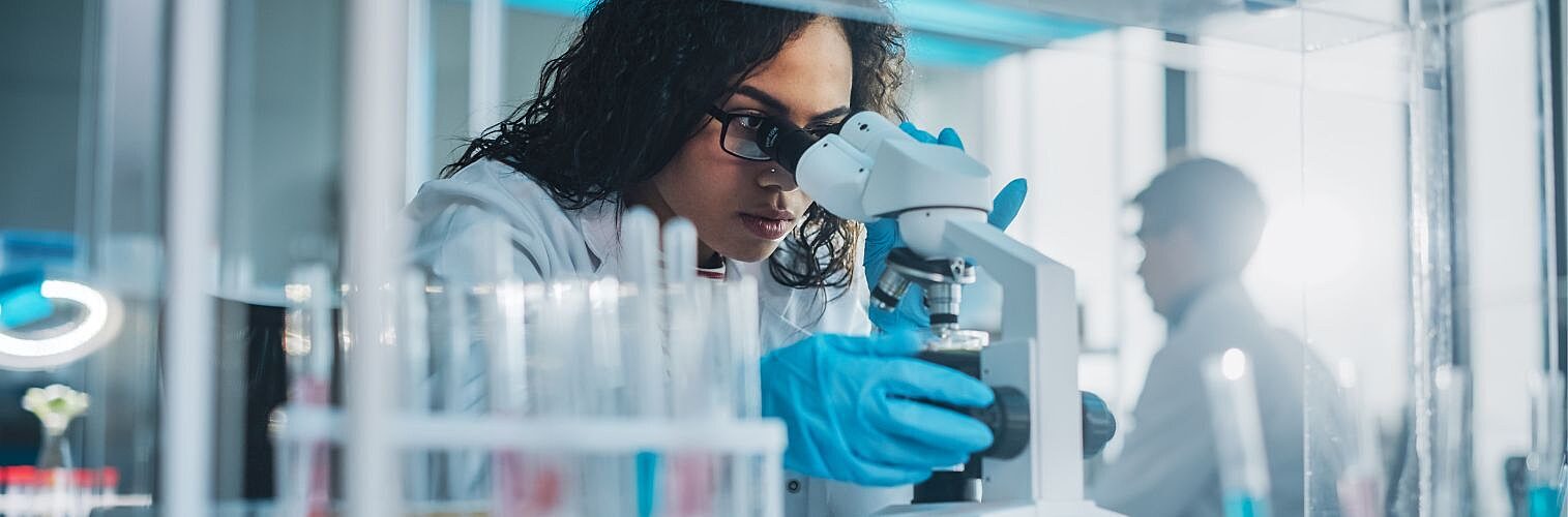 Scientist looking under microscope does analysis of test samples.