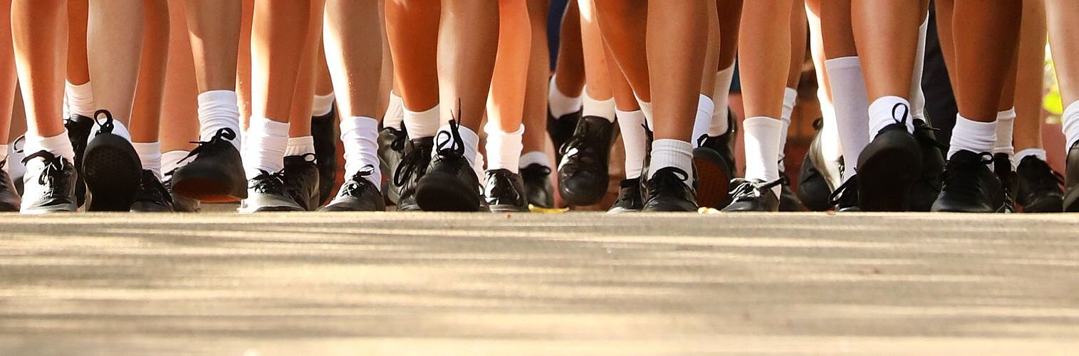 Many legs wearing school uniform of white socks black shoes and tartan skirt.
