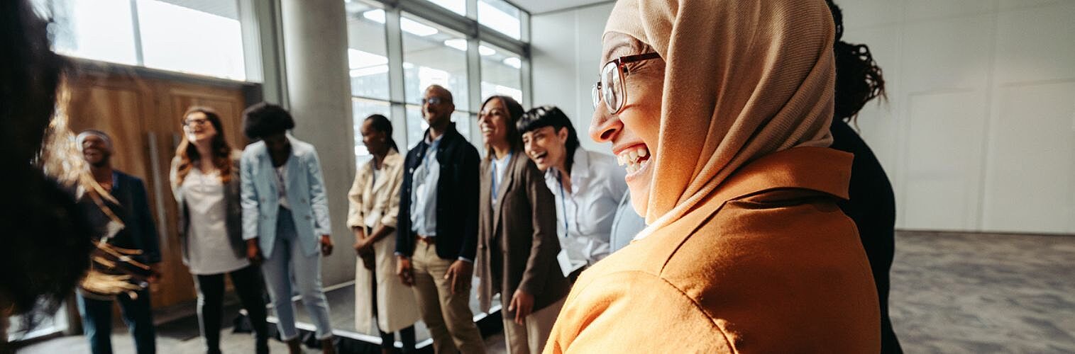 A diverse group engages in a bonding activity, with a Muslim woman laughing in a circle during a workshop.