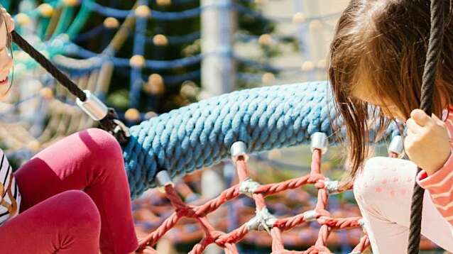 Two little girls swinging at the playground on a summer day.
