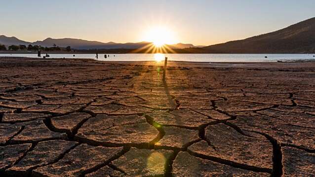 The sun sets setting over a dried, cracked lake bed.