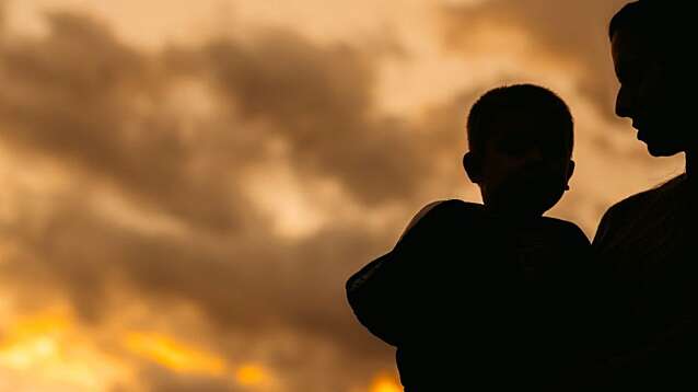 Silhouette of a beautiful young mother holding her son in her arms in the park in autumn.