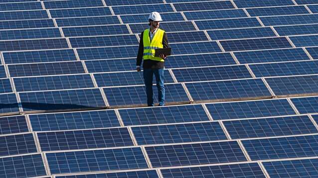 An engineer wearing hard hat and safety vest standing on a solar panel field.
