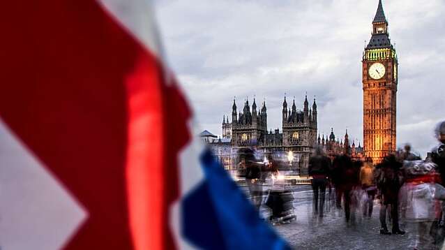 A Union Jack fluttering in front of Big Ben on a bridge.