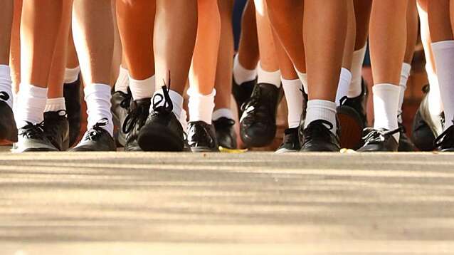 Many legs wearing school uniform of white socks black shoes and tartan skirt.