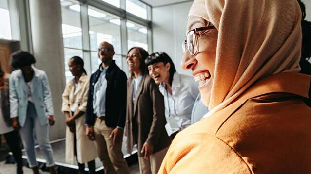 A diverse group engages in a bonding activity, with a Muslim woman laughing in a circle during a workshop.