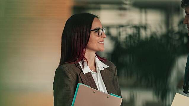 Female teacher and young male student having a candid discussion and sharing insights while standing in a modern school hallway.