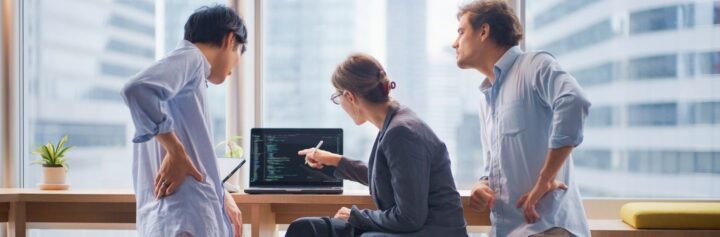 A team of consultants looking at a laptop screen full of code.