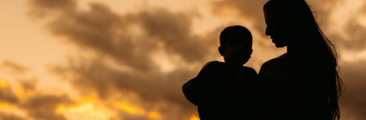 Silhouette of a beautiful young mother holding her son in her arms in the park in autumn.