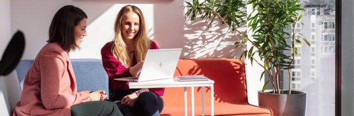Two women sitting on a couch looking at a laptop