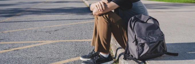 Teenage boy sitting on footpath and looking away from the camera