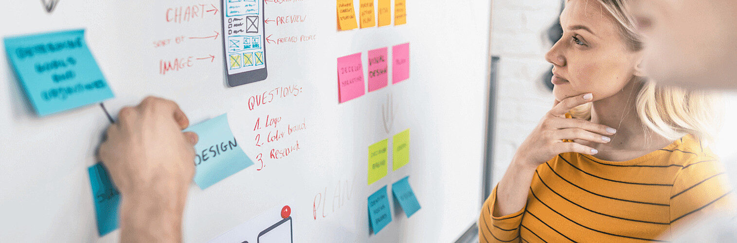 Two people adding sticky notes to a whiteboard