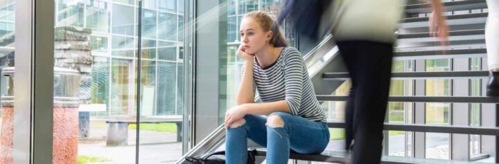 A university student sitting on a staircase while other people pass by
