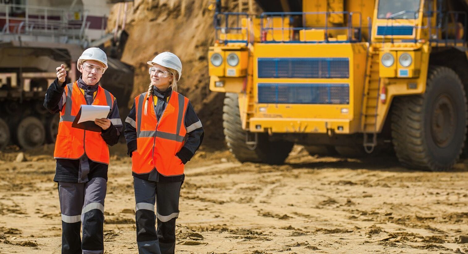 Two individuals wearing high-vis clothing walking on a mining site